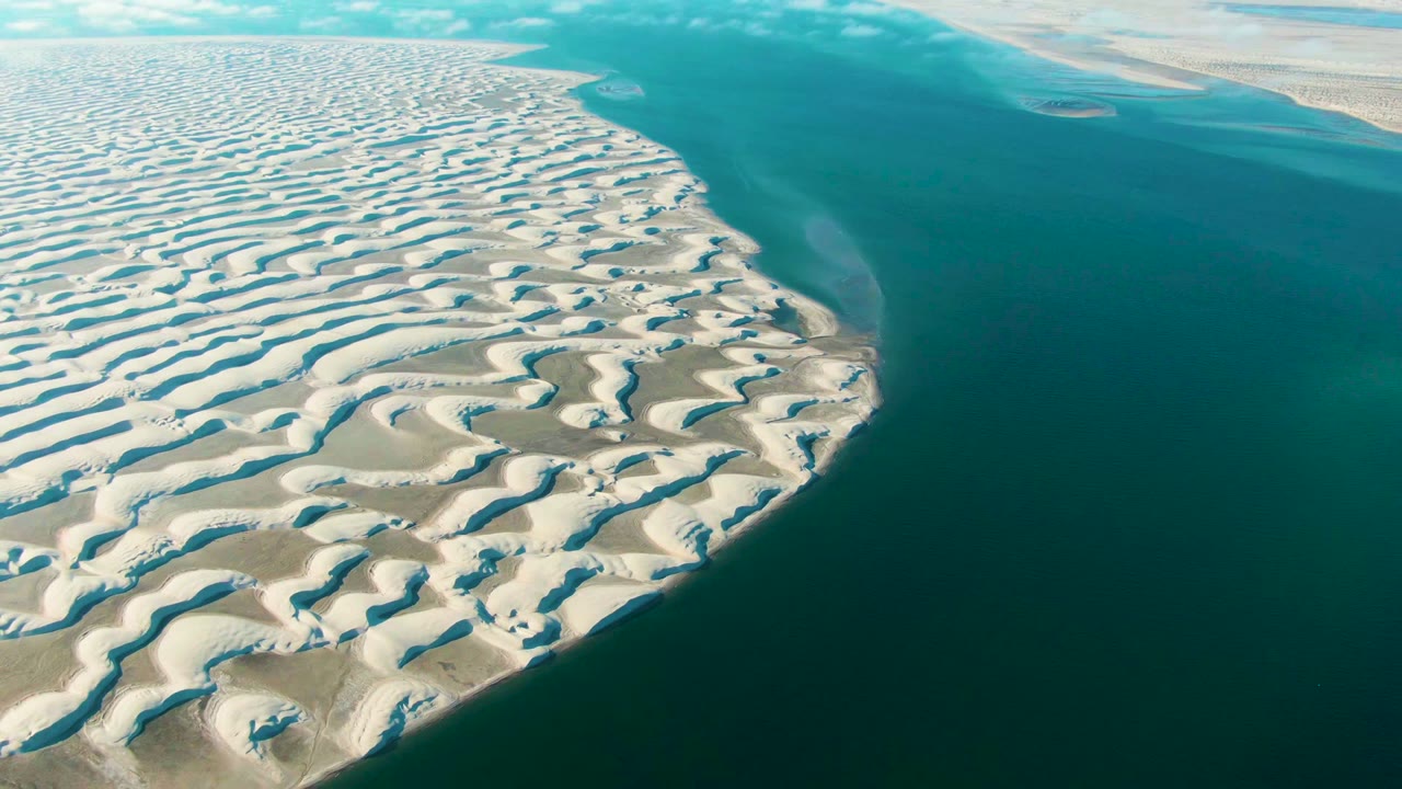 Patterned white dunes curve along deep blue-green water.