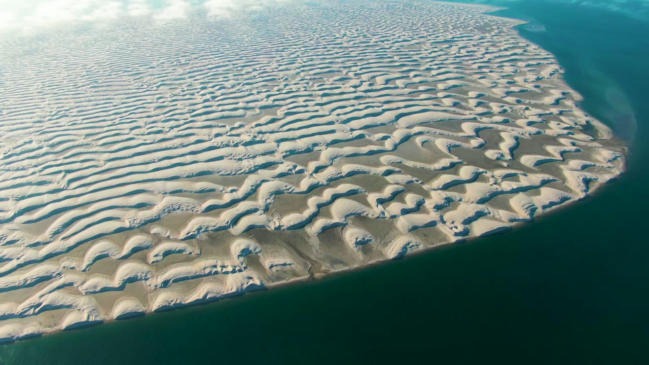 Aerial view over rippled sand bars and teal ocean water in Guerrero Negro, Baja California Sur, with soft light and no visible people.