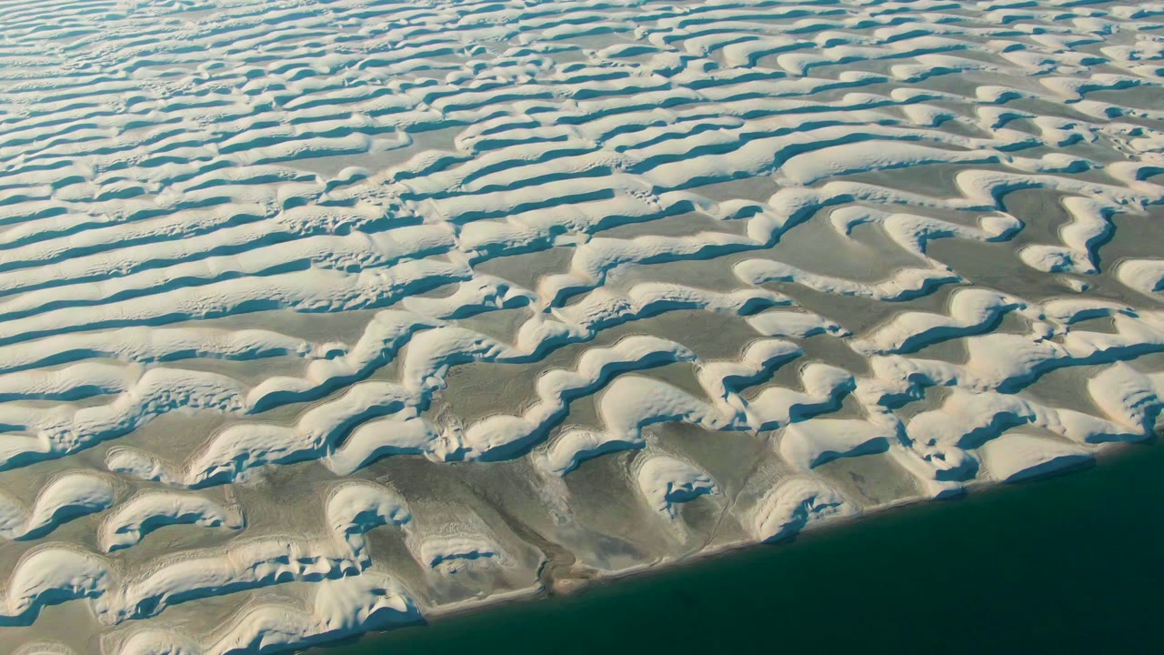 White sand ridges curve toward a dark shoreline band.