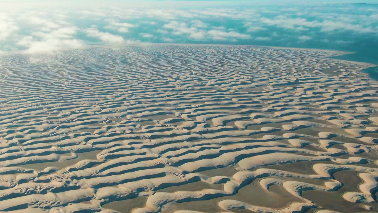 Opening aerial frame over rhythmic sand dunes near Guerrero Negro, Baja California Sur, with a low clouded horizon and no visible people.
