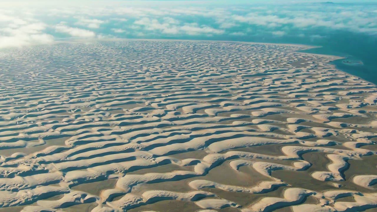 Opening aerial frame over wavy sand dunes in Guerrero Negro, Baja California Sur, with water on the right horizon and no visible people.