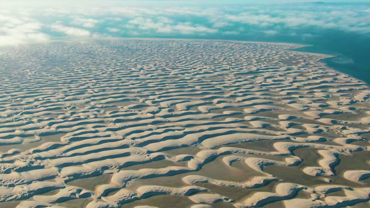 Patterned sand dunes stretch toward water and a cloudy horizon.