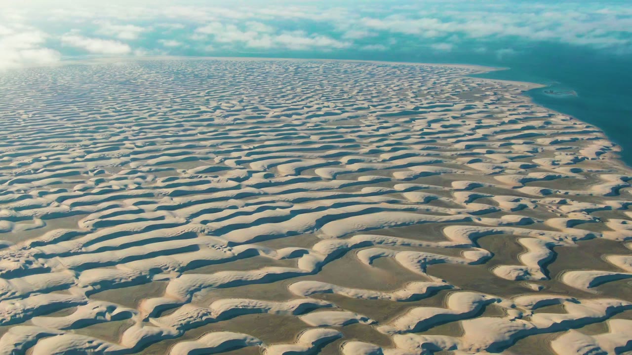Aerial coastline with repeating dune ridges and ocean at right.