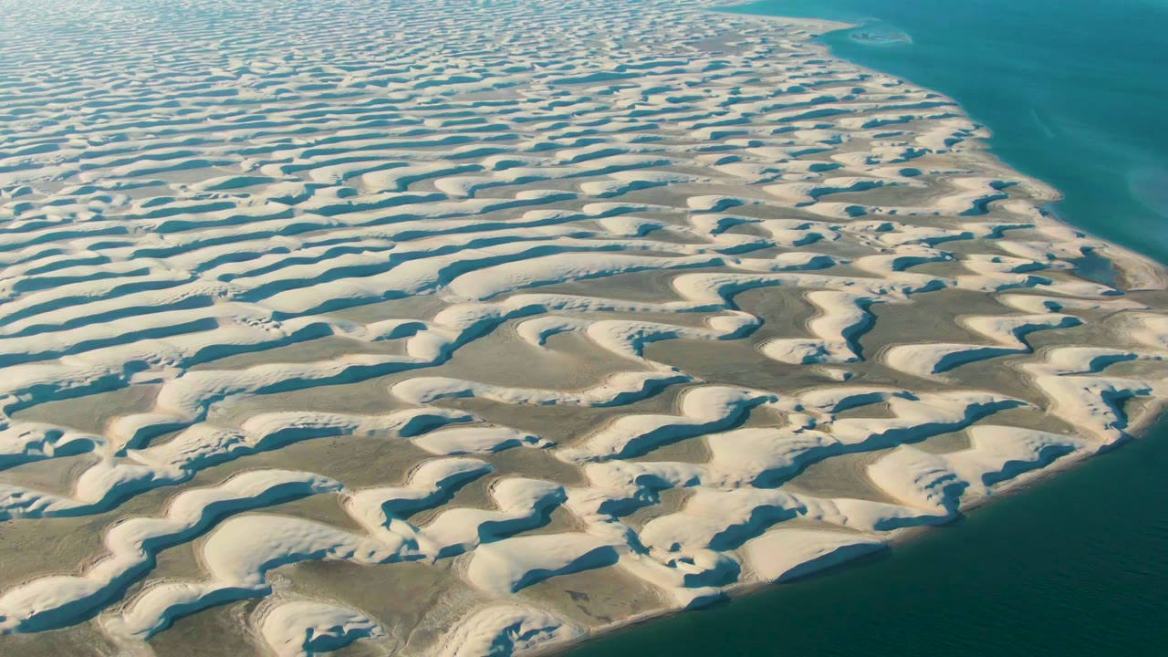 Aerial frame over Guerrero Negro, Baja California Sur, showing pale wavy sand dunes beside deep blue water with no visible people.