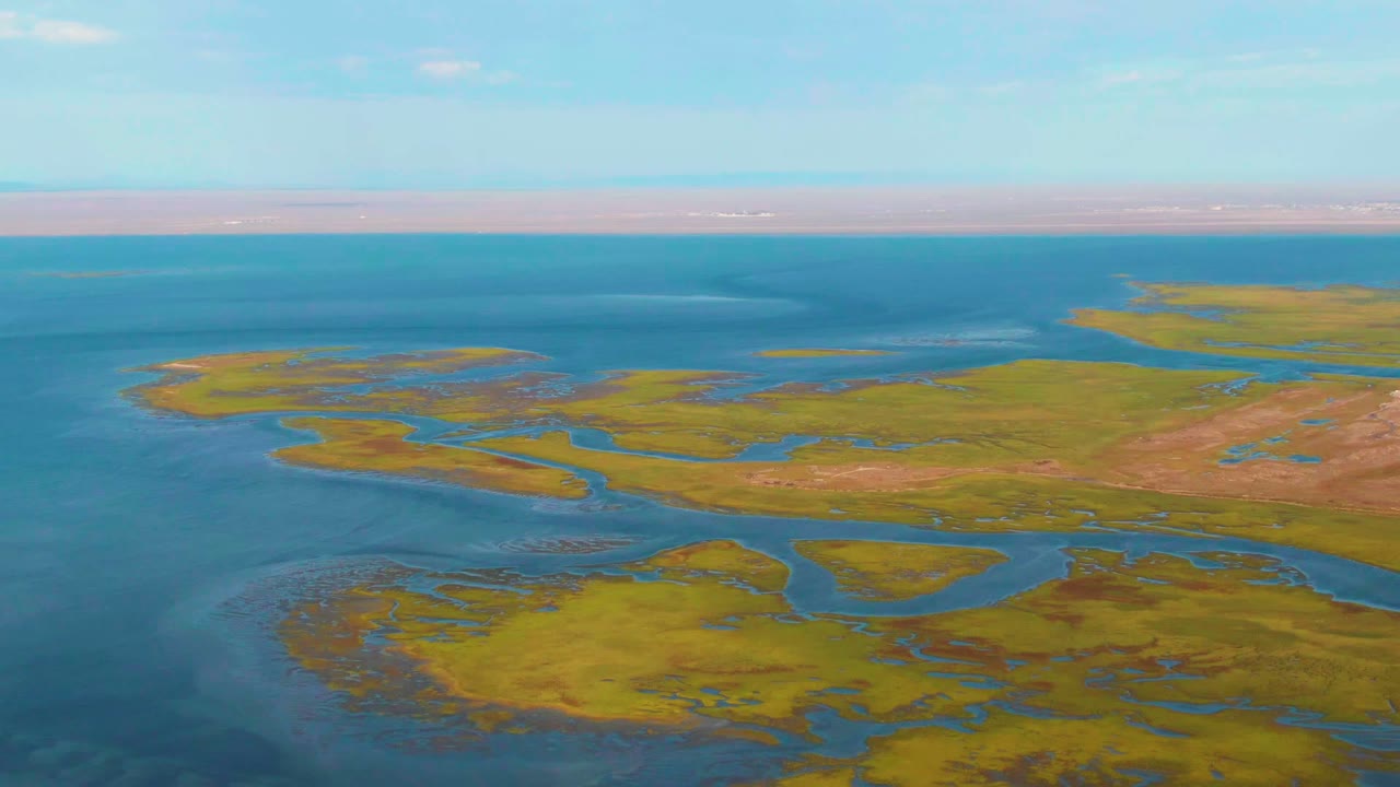 Aerial view over Guerrero Negro wetlands with green marsh islands, branching blue channels, open water at left, distant shoreline, and no visible people.