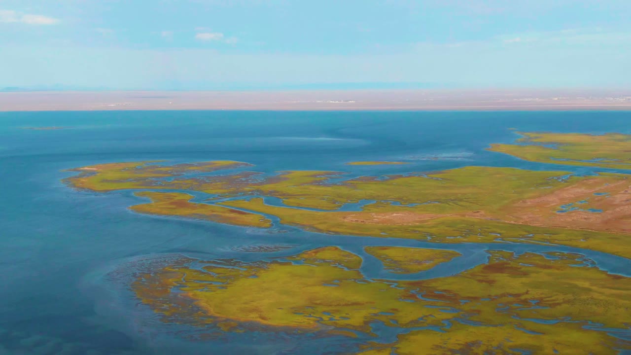 Green marsh terrain divided by blue waterways under a clear sky.