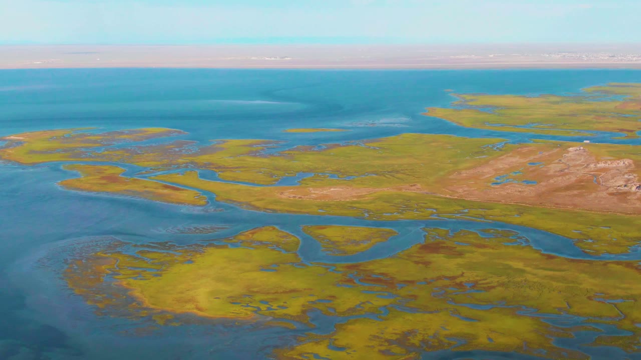 Aerial view over Guerrero Negro, Baja California Sur, Mexico, showing green marsh islands cut by blue tidal channels with brown earth flats, open water, clear sky, and no visible people.
