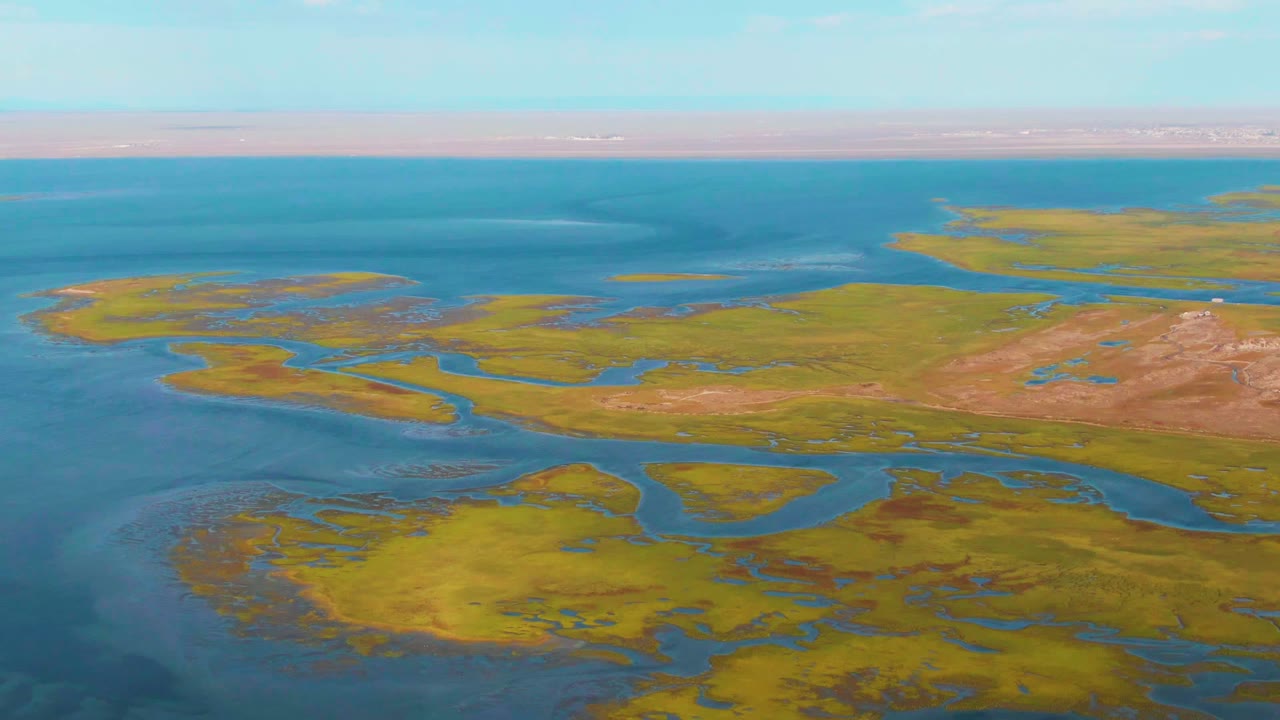 Aerial frame from Guerrero Negro showing marsh islands surrounded by blue water, shallow channel patterns in the foreground, brown flats on the right, and no visible people.