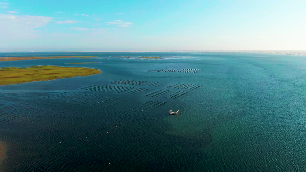 Wide drone view of coastal water with fish farm rows and small boats.