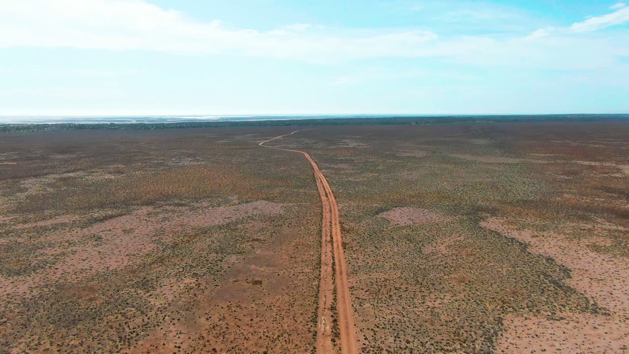 Aerial view in Guerrero Negro, Baja California Sur, with the reddish road slightly right of center as it narrows toward the horizon across an arid plain, no visible people.