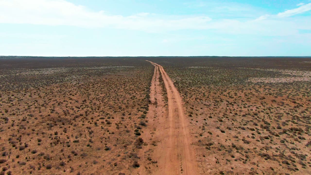 Straight dirt road through dry scrubland under a bright sky.