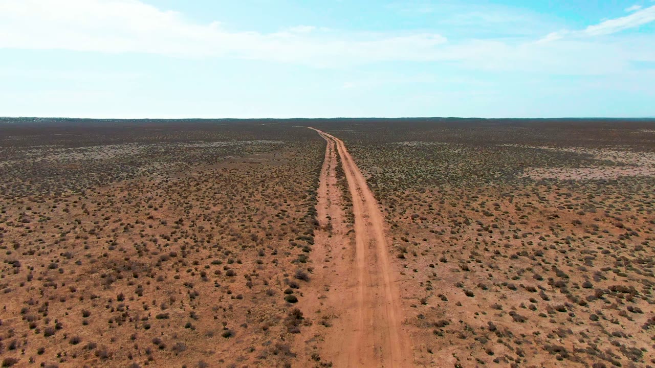 At 0:02, an elevated view shows the reddish road stretching into the distance across dry Guerrero Negro terrain, with scattered shrubs and no visible people.