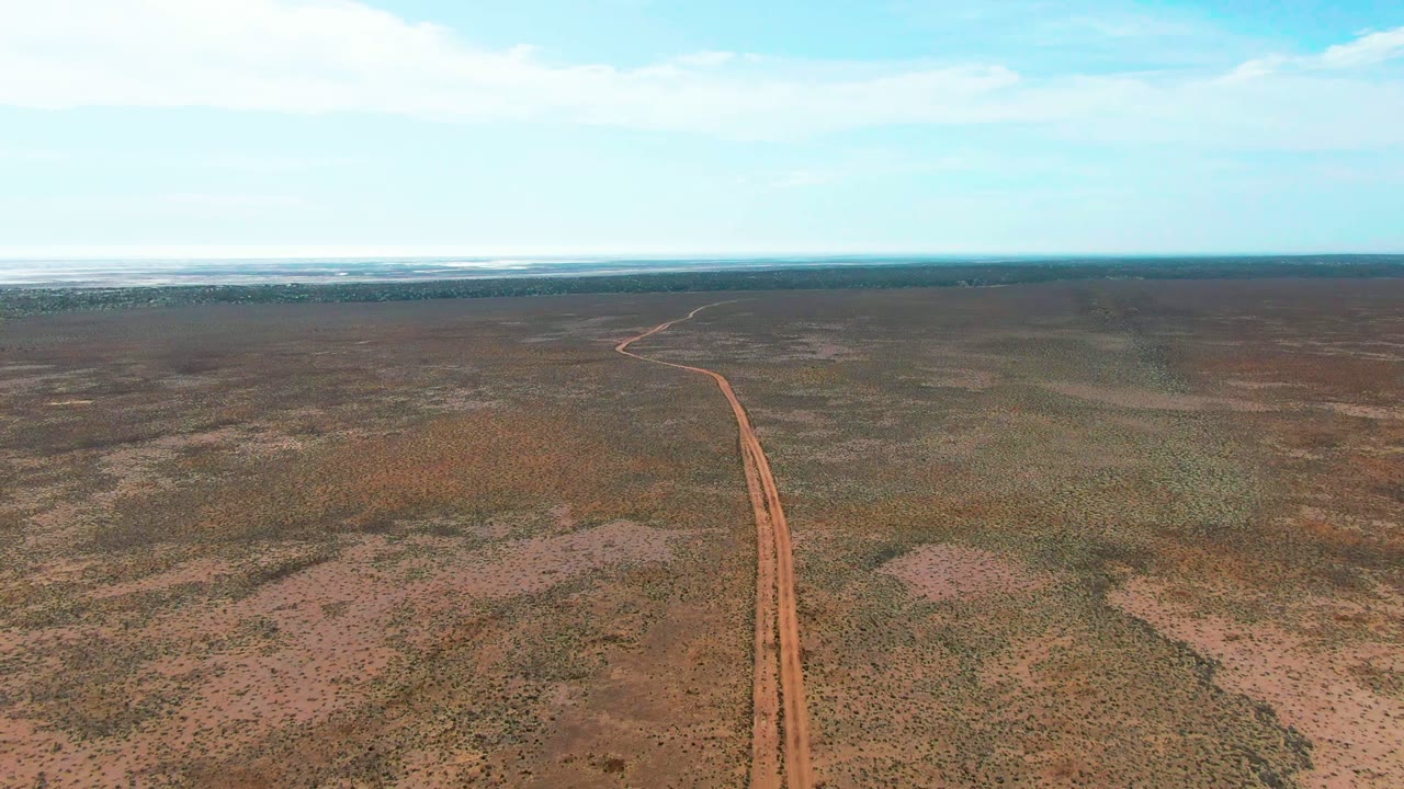 At the start of the Guerrero Negro clip, a red dirt road enters from the lower left and runs toward a distant horizon across flat arid scrubland, with no visible people.