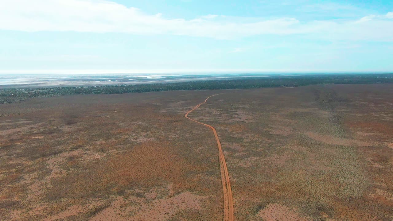 High aerial view of a dirt road bending through dry flat plains below a bright sky.