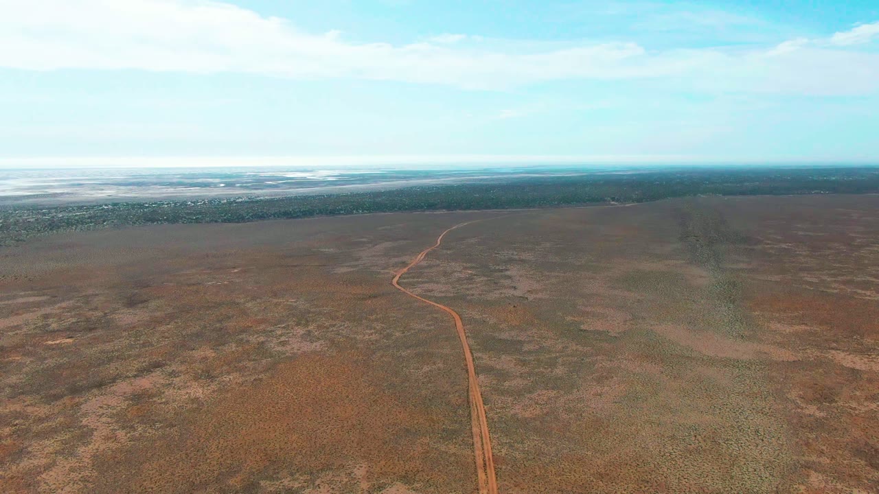 Aerial frame from Guerrero Negro, Baja California Sur showing a reddish dirt road entering from the lower center and running into dry brown plains, with no visible people.