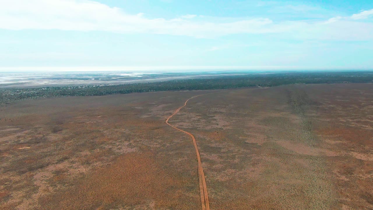 High aerial view of a winding red dirt road through open scrubland.
