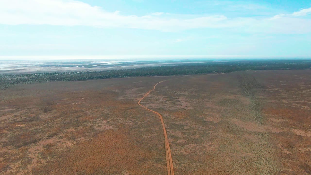 Aerial frame from Guerrero Negro, Baja California Sur where the dirt road curves gently through the midground toward a dark horizon band, with no visible people.