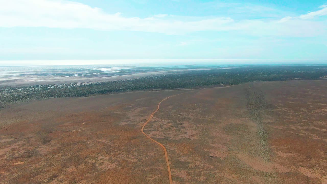 High aerial view of a curved dirt road in a broad arid plain.