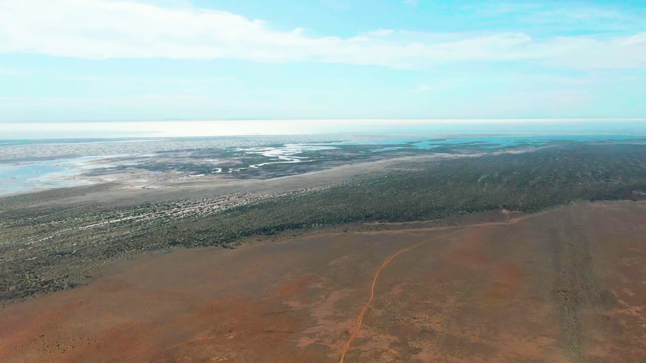 High aerial view across reddish plain toward coastal vegetation and shallow water.