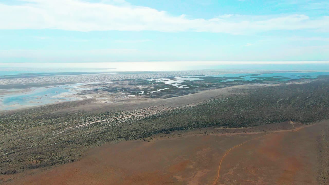 High aerial landscape with red soil, scrubby green land, distant water, and clouds.