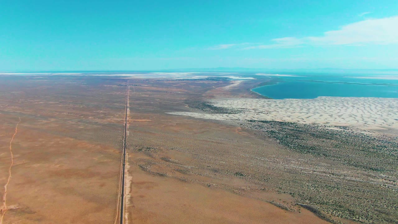 Straight desert road leading toward white salt flats and water
