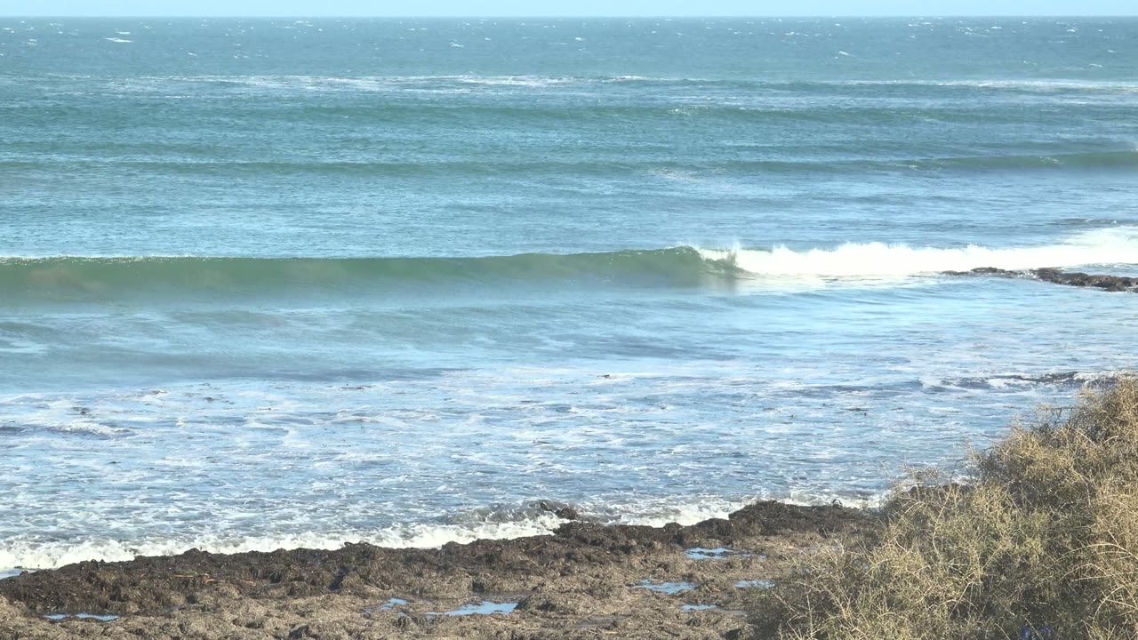 Wide surf line breaking across blue water.