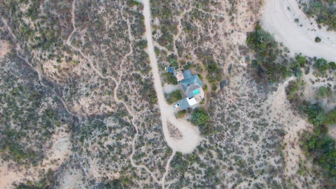 Aerial view of a dirt road curving past scrub and a small structure.