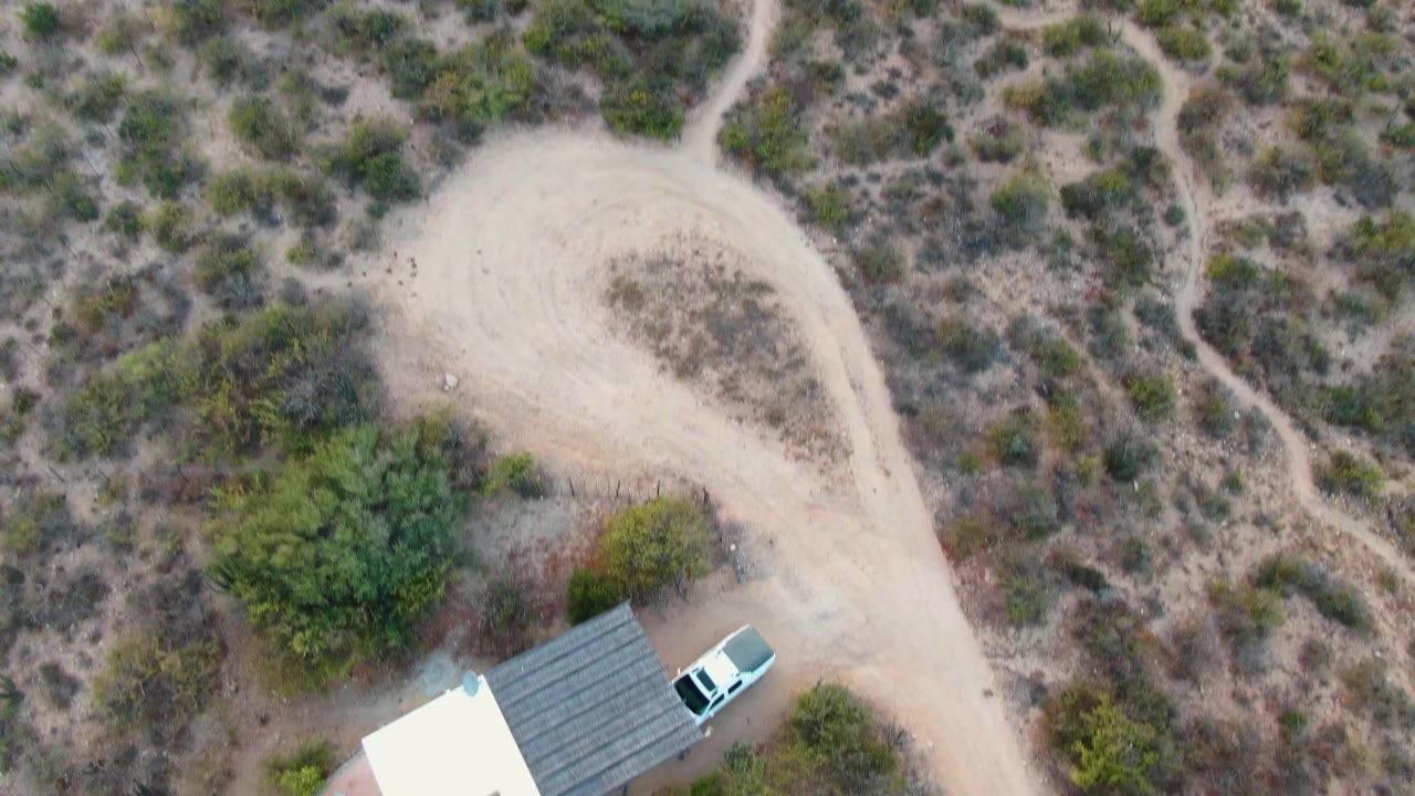 Overhead view of a house edge, white vehicle, dirt road, and desert scrub.