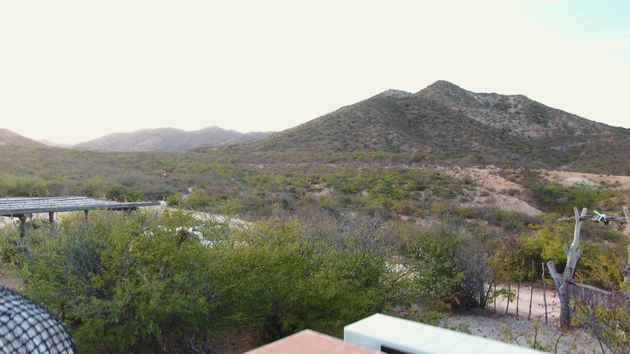 Desert landscape with carport edge, white car, shrubs, and mountains.