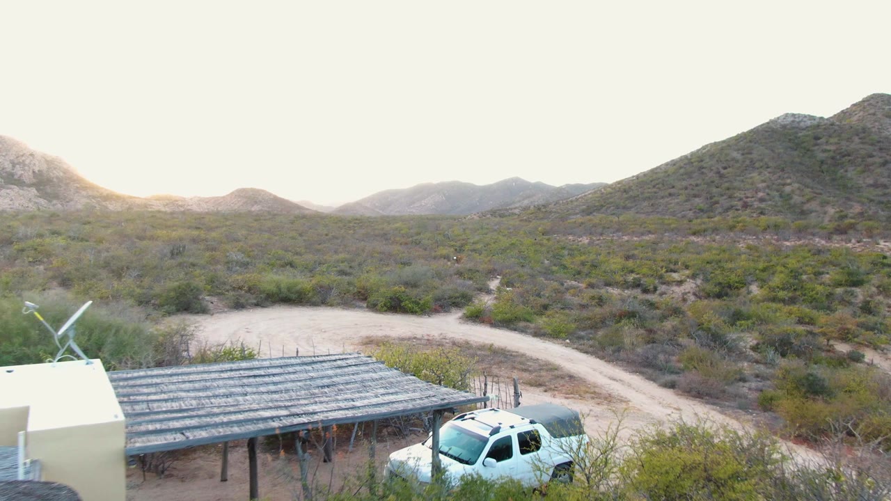 Desert road, carport, white truck, and mountains under bright sky.