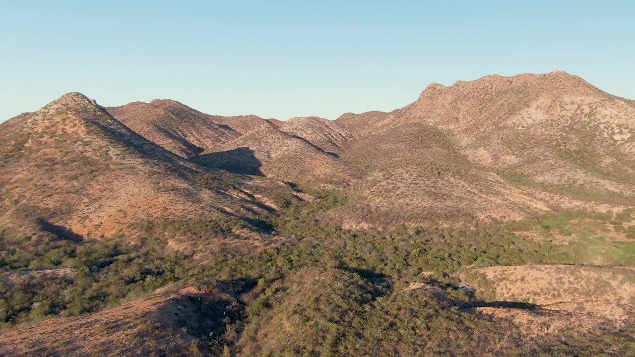 Sunlit arid hills with sparse green vegetation and a mountain ridge across the horizon.