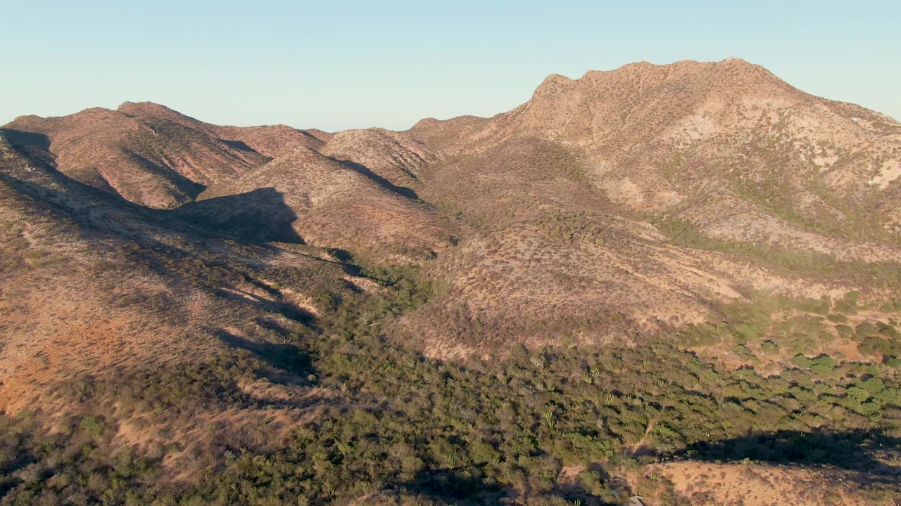 Closer aerial view of brown mountain slopes and dense green brush in the foreground valley.