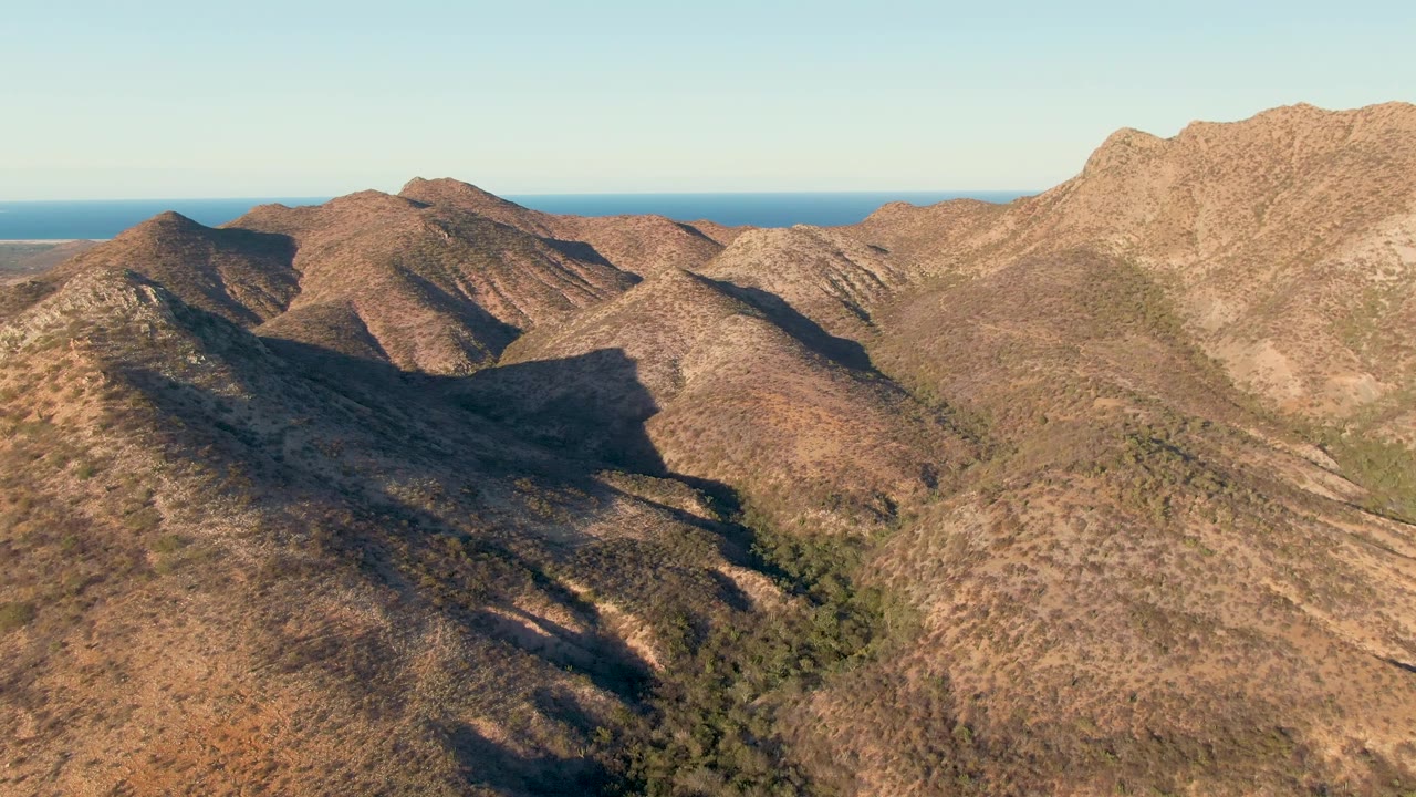 Dry mountain ridges with distant blue ocean horizon.