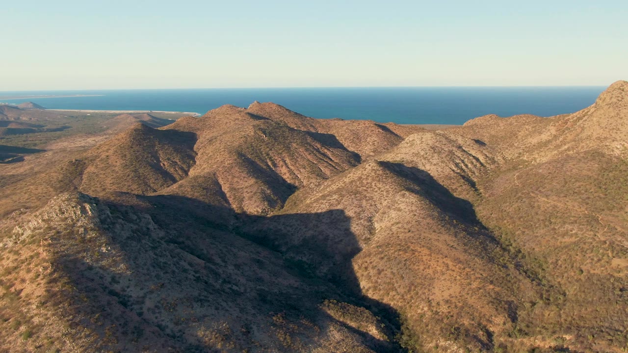 Aerial view of dry mountain ridges with ocean beyond.