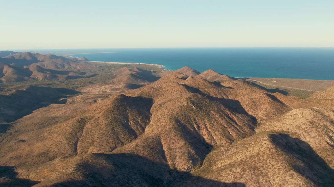 Aerial view of brown mountain ridges with blue ocean beyond