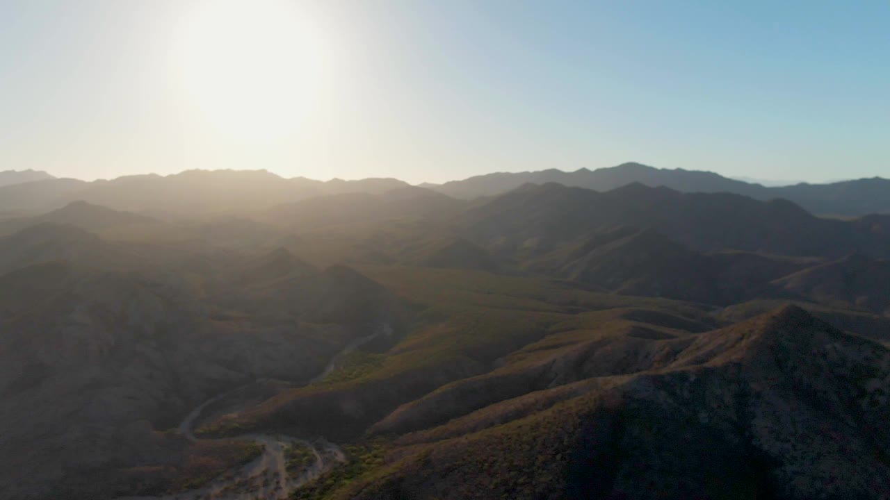 The eagle has left view, leaving a broad Cabo Pulmo mountain panorama with strong sun glare, dry ridgelines, a pale road, and no visible people.