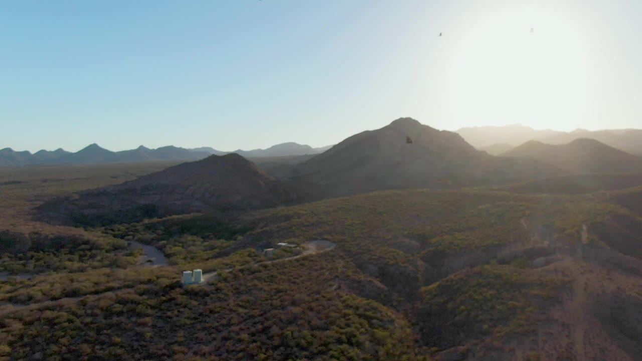 Desert mountains and valley under bright sun with a dirt road below.