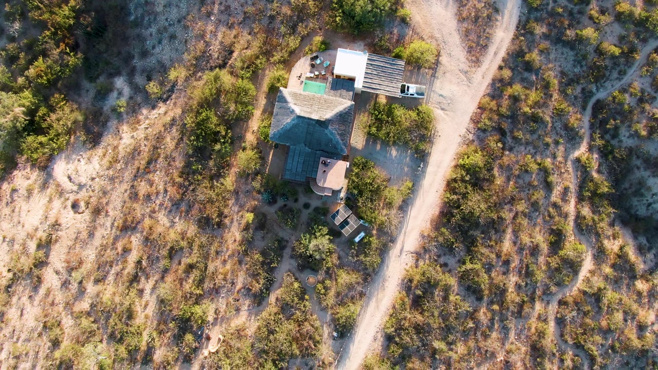 Top-down view of a house, white truck, and dirt road through dry vegetation.
