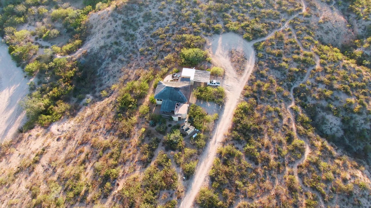Drone view of the hillside home, driveway, and scrub-covered slopes.