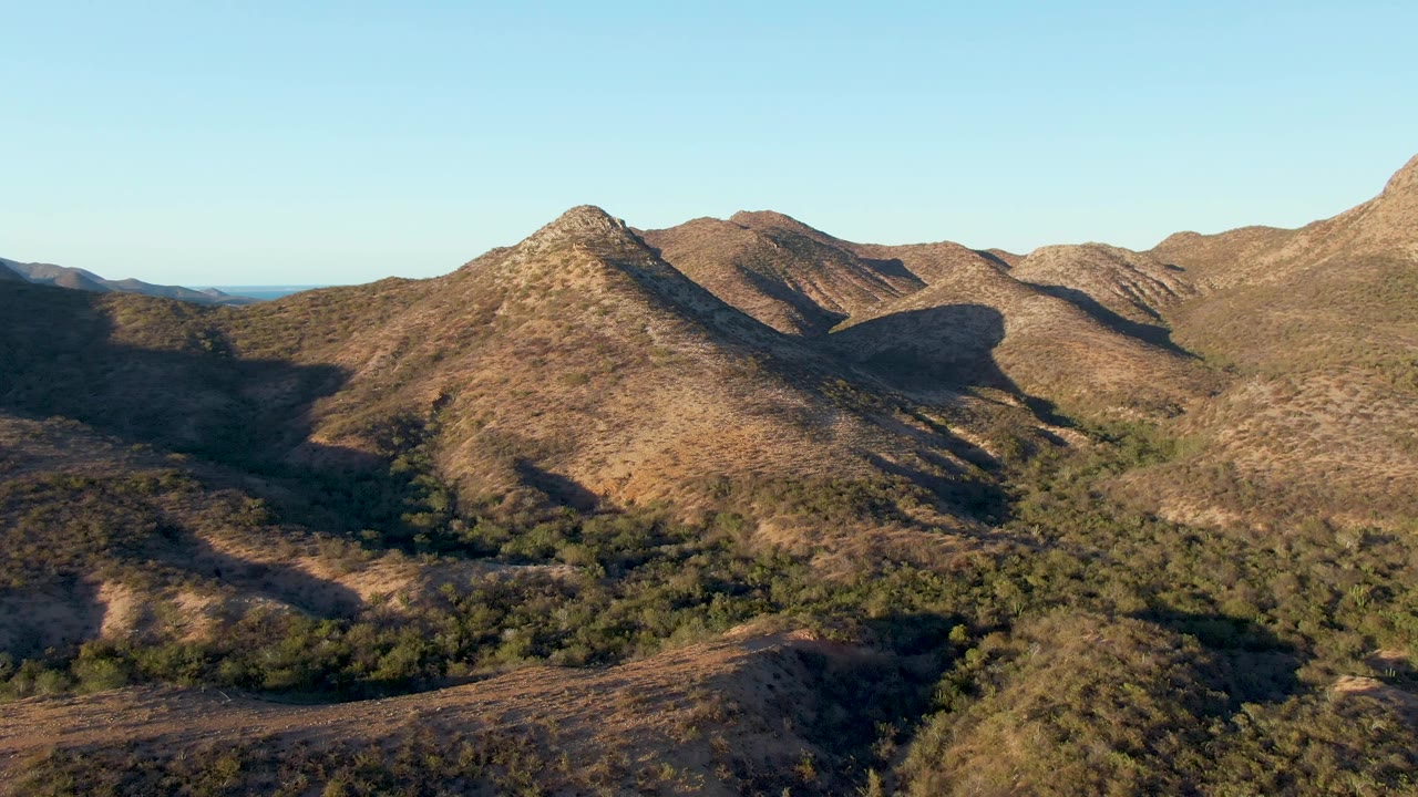 Aerial view of dry hills with scattered green vegetation and blue sky.