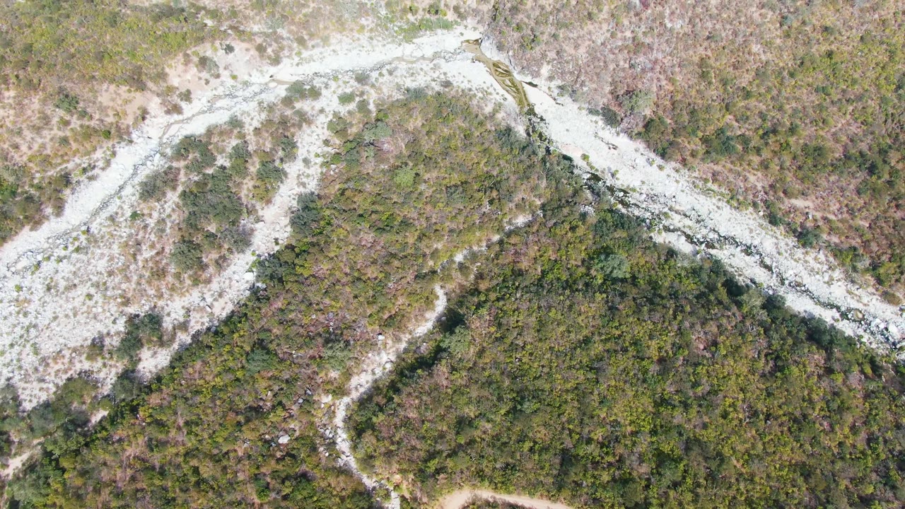 Aerial frame from San Dionisio, Baja California Sur with a small vehicle near the upper road bend, surrounded by scrub-covered slopes and no visible people.
