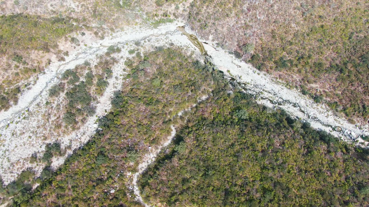 Pale dirt road snakes between scrub-covered hills from above