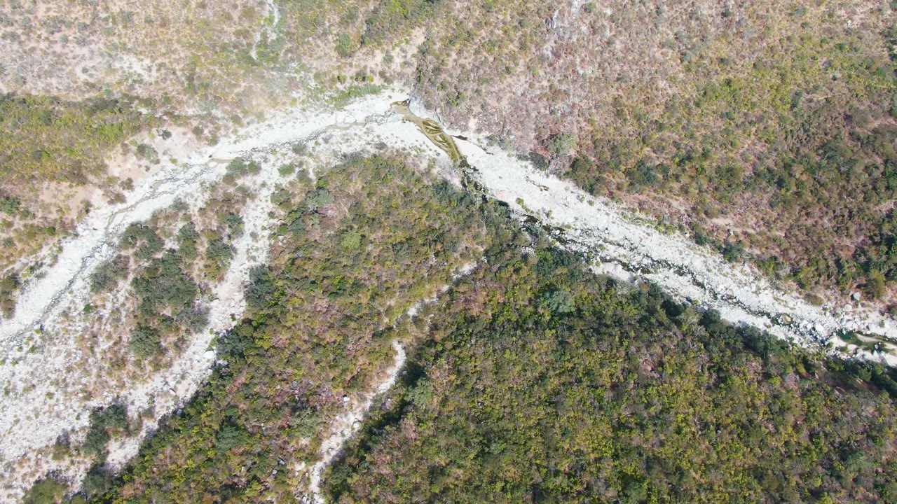 High aerial frame over San Dionisio, Baja California Sur, showing a pale winding mountain road cutting through green and brown scrubland with no visible people.