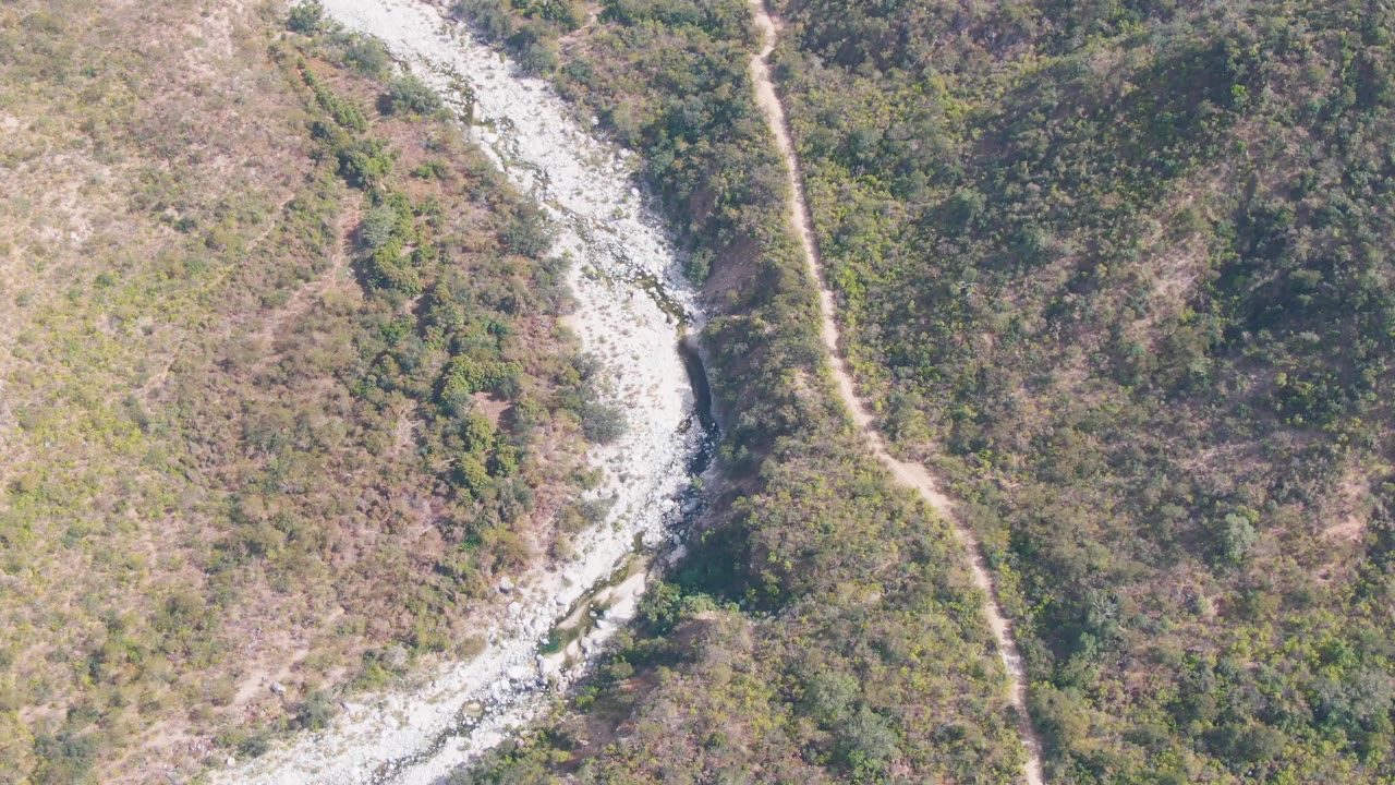 Aerial view of a pale river channel and footpath through mixed brush.
