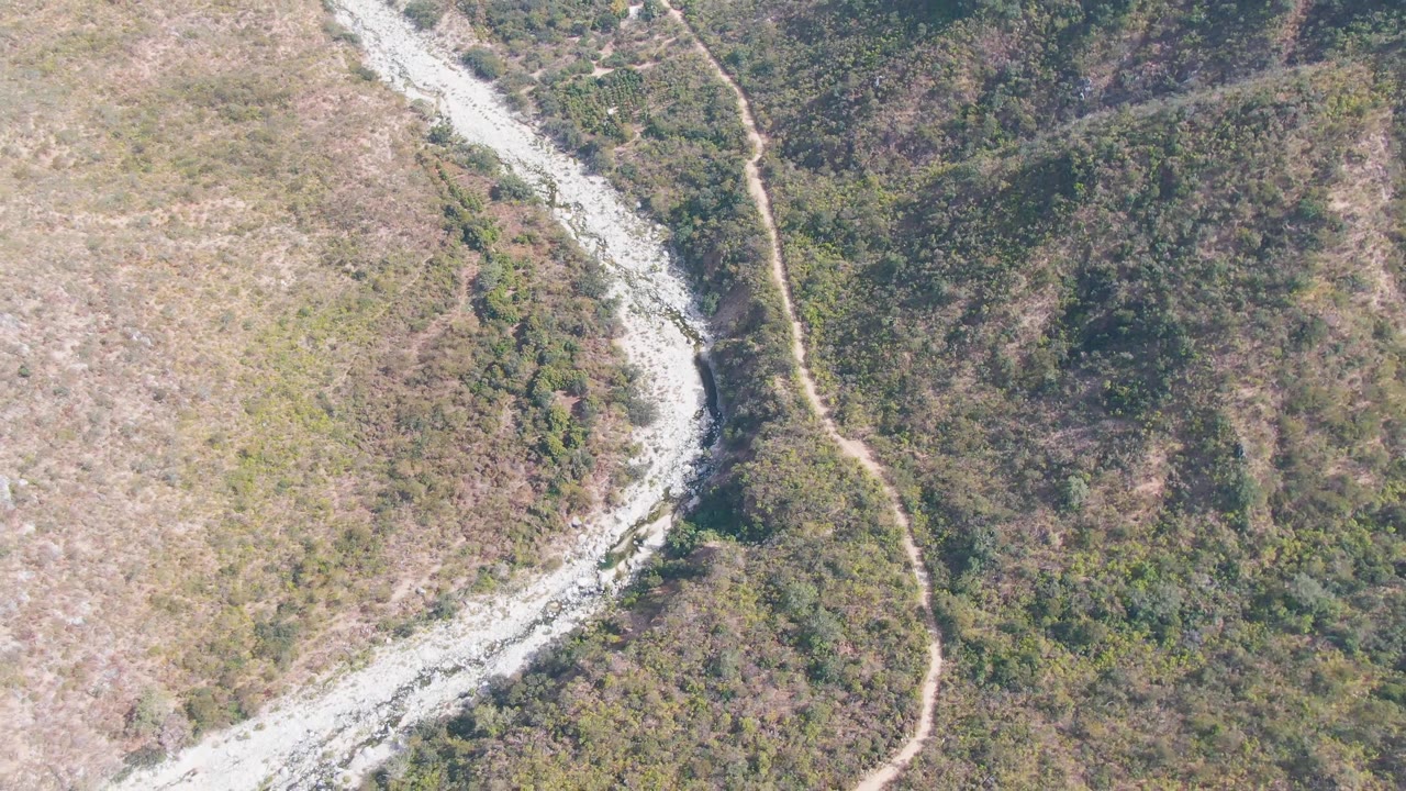 Aerial view of a curved rocky wash with dirt road through mixed vegetation