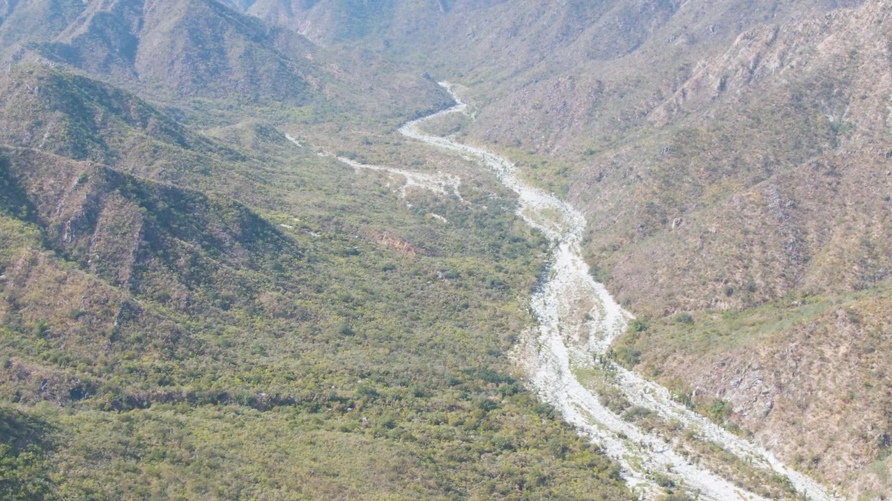 Aerial view of a bright riverbed bending through a dry mountain valley.