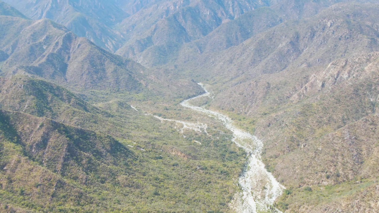 Aerial view in San Dionisio, Baja California Sur with the river more centered between scrubby green valley floor and steep brown slopes, with no visible people.