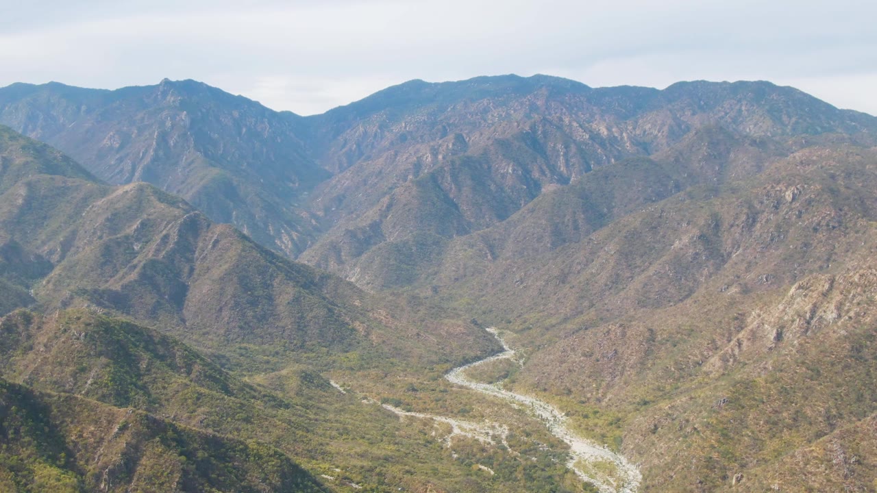 Wide aerial view of a winding riverbed between dry green-brown mountains.
