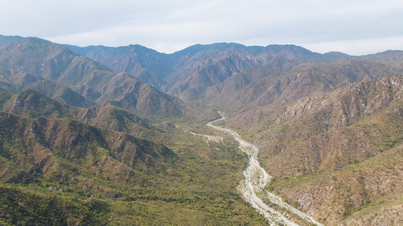 San Dionisio aerial view with the river bend centered lower in frame, rocky slopes on both sides, layered mountains beyond, and no visible people.