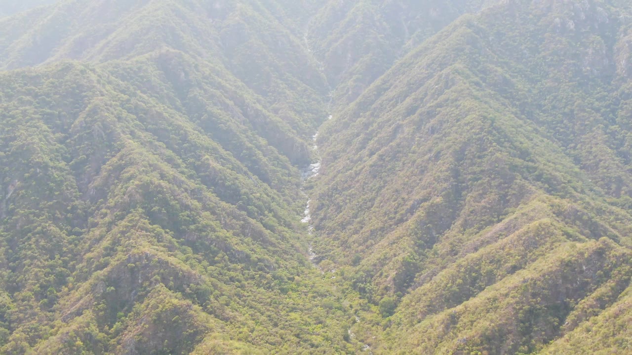 San Dionisio aerial view with rounded green and brown slopes surrounding a thin bright river channel, with no visible people or structures.
